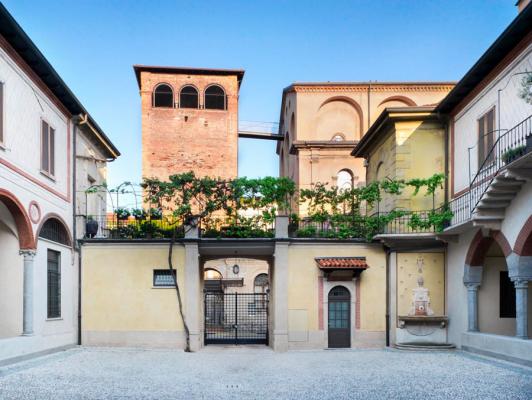 cortile edificio medievale con terrazzo con piante, portico e torre in lontananza