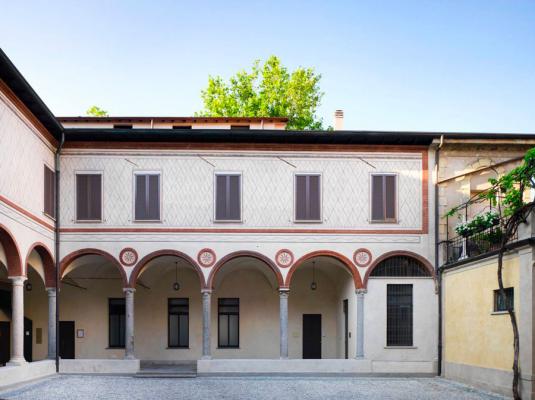 cortile interno edificio medievale con porticato coperto, finestre alte e strette, terrazzo con piante